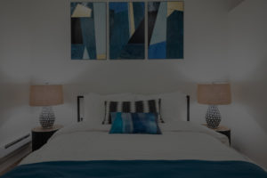 darkened image of a made bed with decorative blue pillows.
